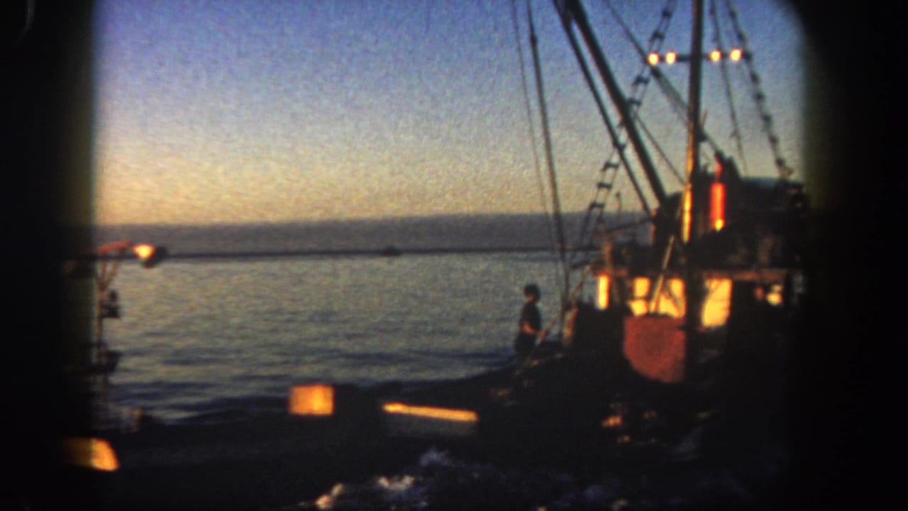 Fishing boat at dusk with a smaller vessel nearby and glowing lights on the water.