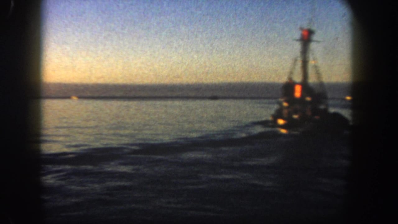 1962 San Diego harbor view with a small fishing boat receding across darkening water at dusk.
