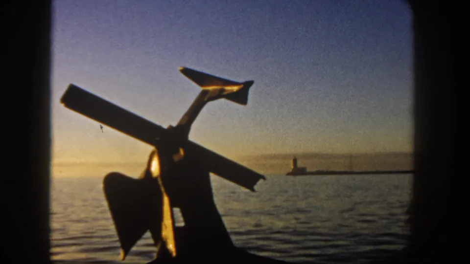 8mm frame from 1962 San Diego showing a silhouetted maritime object against calm water, sunset color, and a distant pier light.