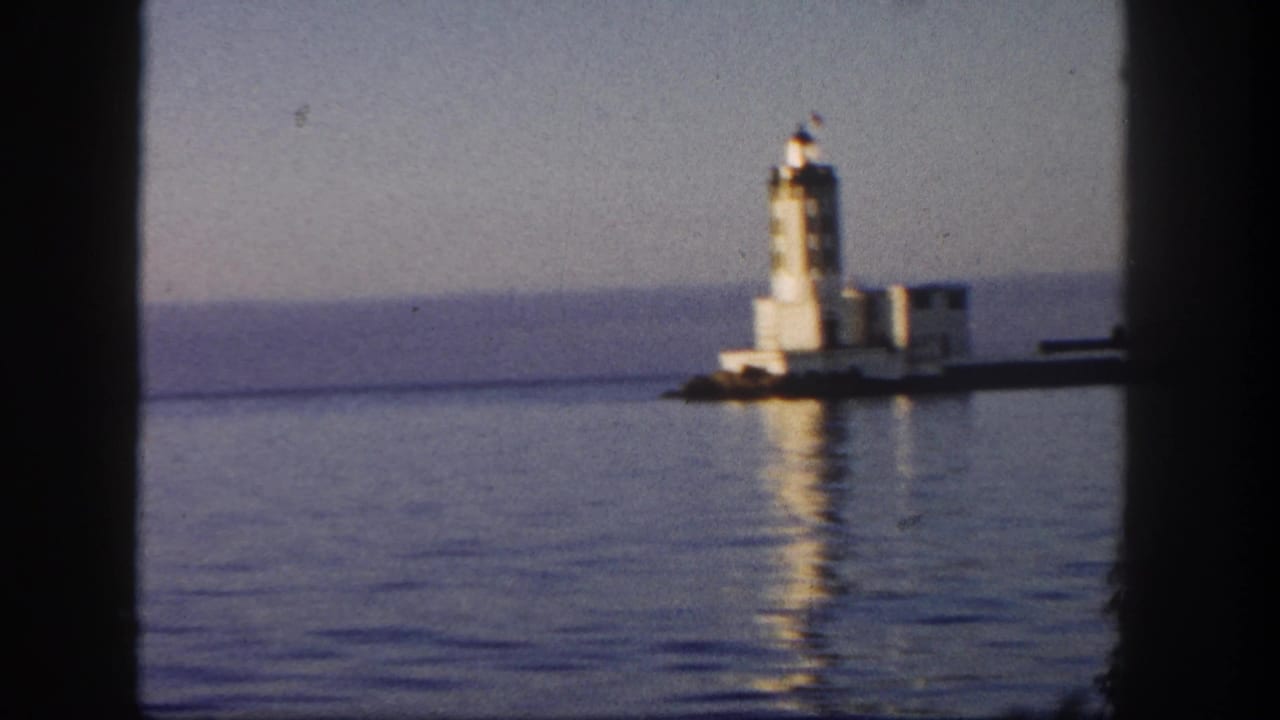 Lighthouse seen across calm water through a boat window frame.