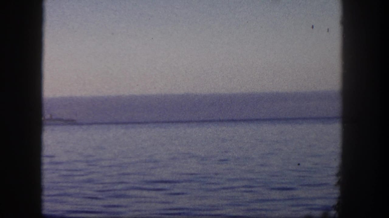 Boat-window view over San Diego water with the lighthouse mostly out of frame and a distant shoreline on the horizon.