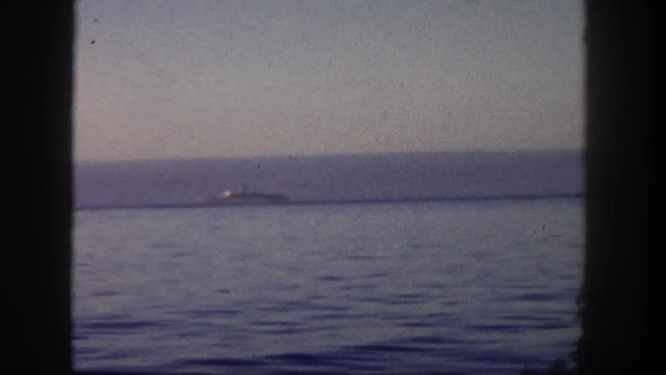 1962 San Diego harbor view with a small distant ship on the horizon, filmed through a dark boat window frame.