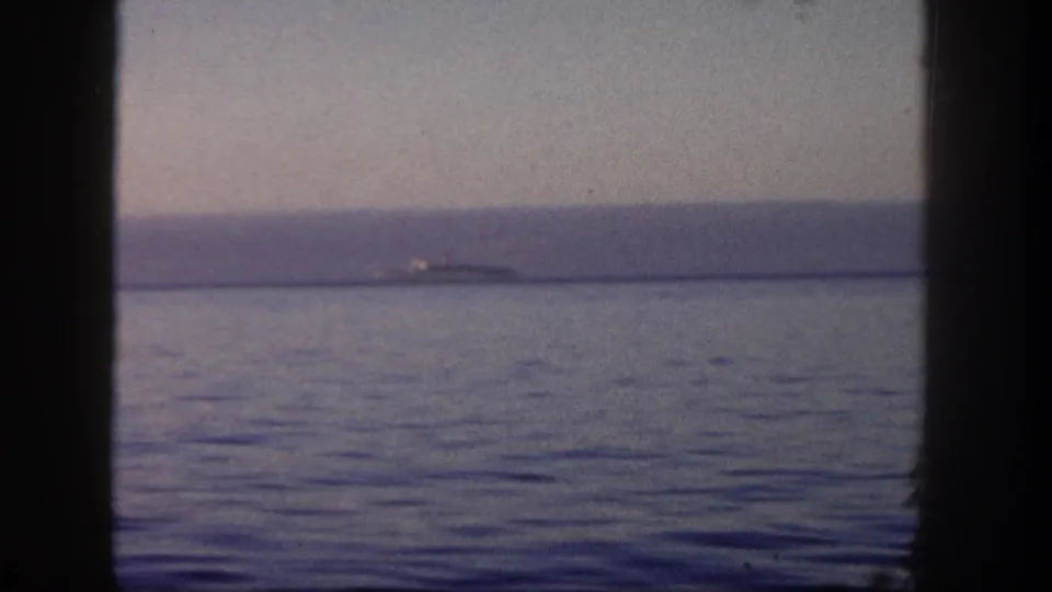 Final 1962 San Diego boat-window frame showing calm water, distant shoreline, and a small bright vessel near the horizon.