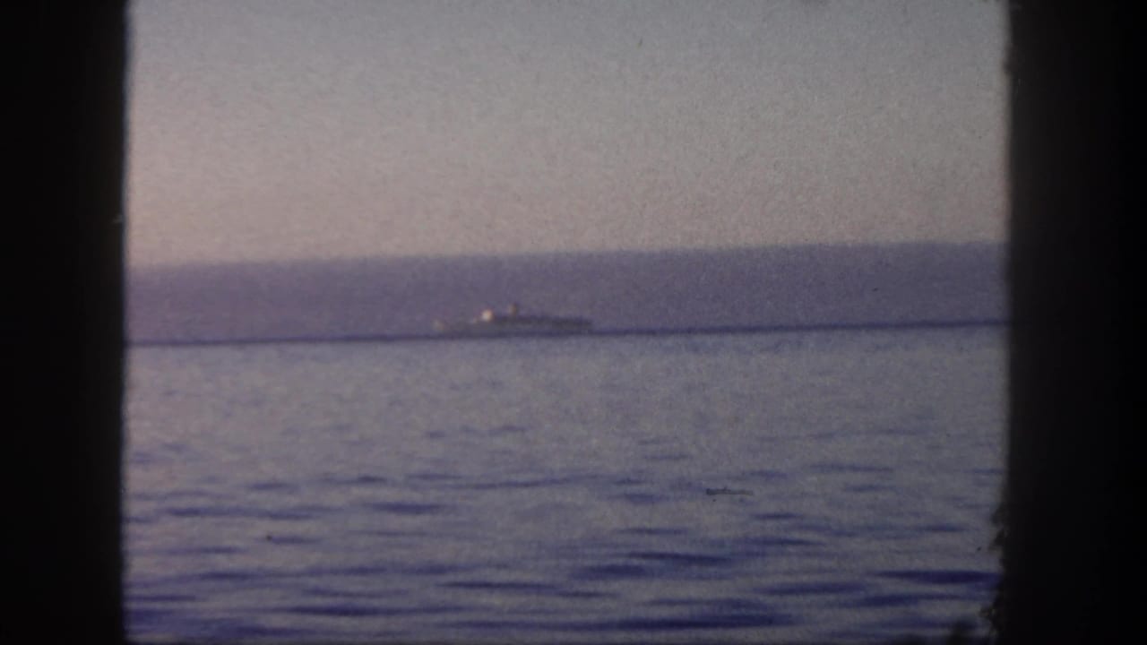 Distant ship shape on calm water seen through dark vertical framing.
