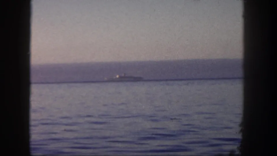 1962 San Diego home-movie frame showing a distant vessel or liner on calm water through a dark window-like frame.