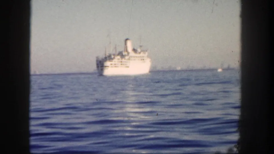 1962 San Diego 8mm frame showing a white ocean liner at distance on calm blue water under a pale hazy sky.