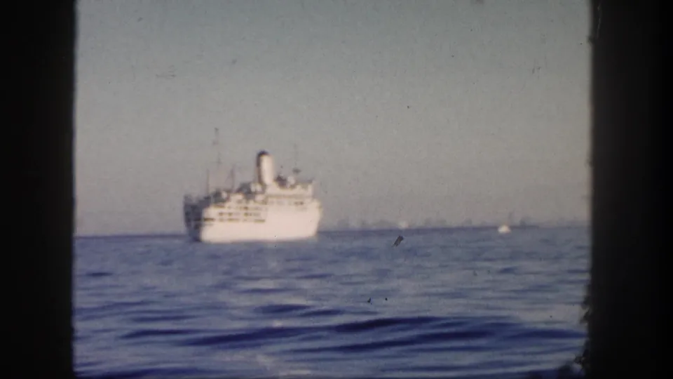 1962 San Diego home-movie view of a distant white ocean liner framed by dark vertical edges over calm coastal water.