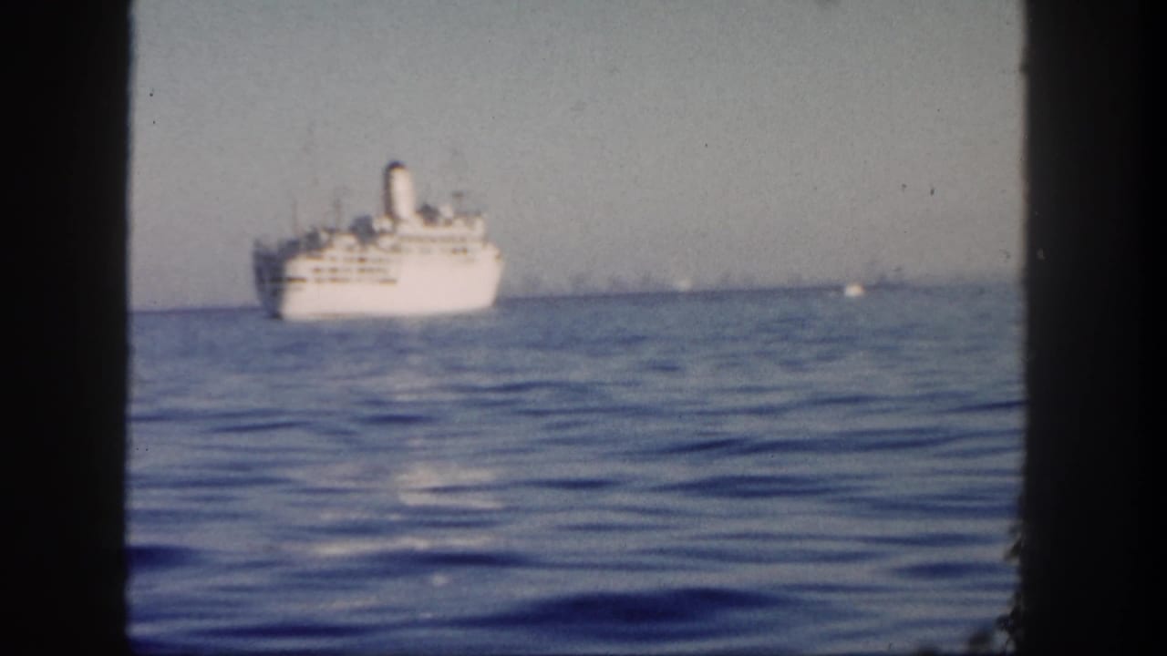 1962 San Diego 8mm frame with a white passenger ship at mid-distance on calm ocean water, partially bordered by the film gate.