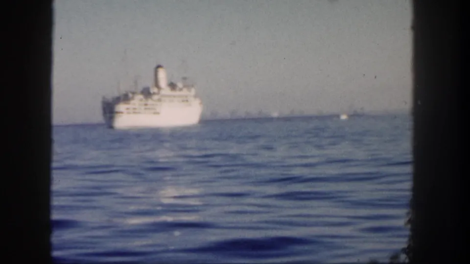1962 San Diego 8mm frame with a white passenger ship at mid-distance on calm ocean water, partially bordered by the film gate.