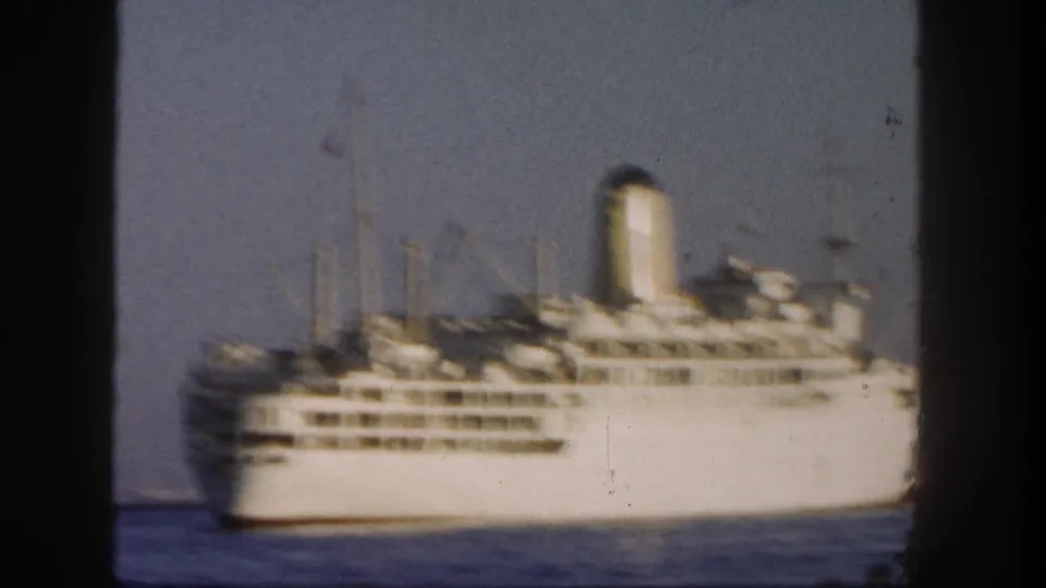 1962 San Diego 8mm frame showing a closer side view of a large white passenger ship with decks, masts, and a funnel visible.