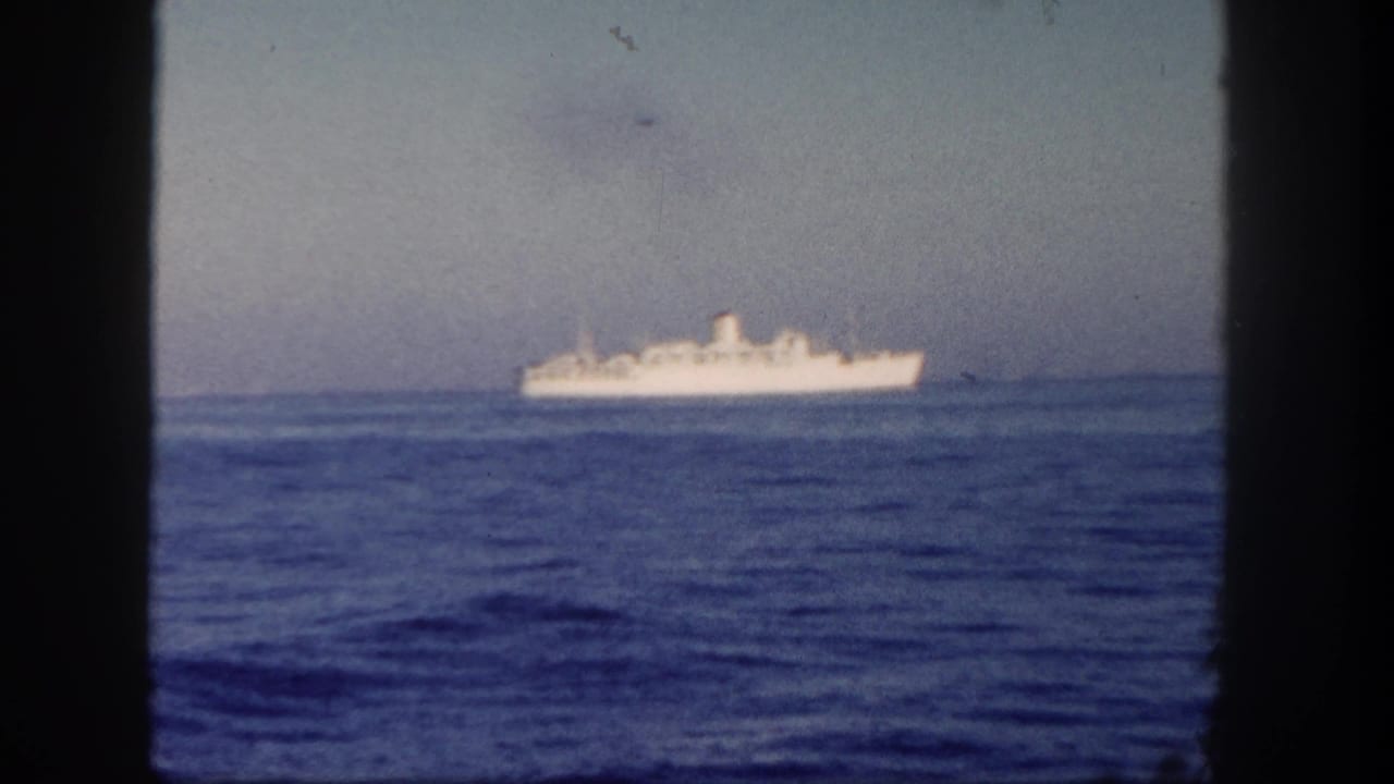 Distant white ship on the ocean seen through a dark window frame.