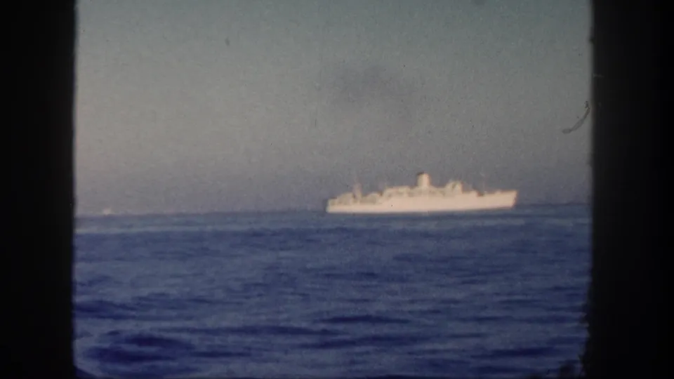 White vessel on the horizon in faded 1962 8mm footage, with dark window edges framing the sea view.