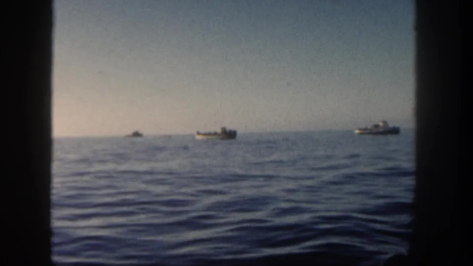 1962 home-movie view from a vessel, with distant boats and a low horizon framed by dark window edges.