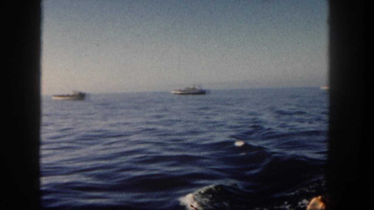 1962 San Diego ocean view from a moving vessel, with distant boats, low horizon, soft focus, and dark 8mm frame edges.
