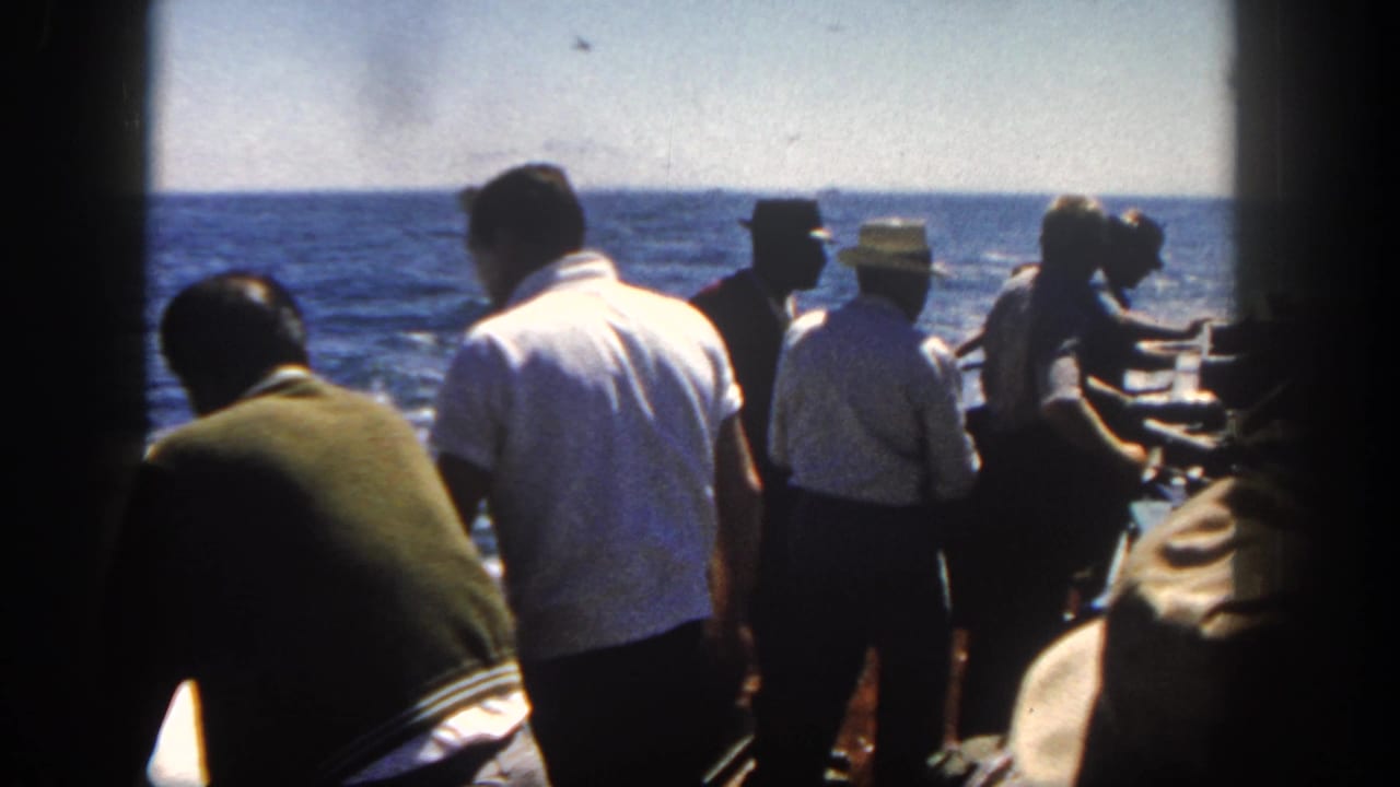 1962 San Diego home-movie frame showing adult men on a boat deck looking toward open water with equipment around them.