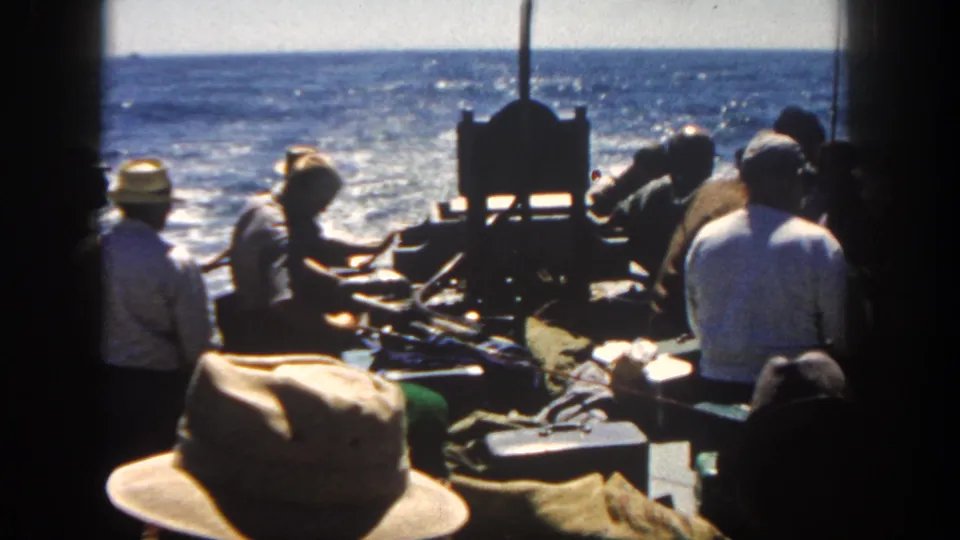 1962 San Diego boating scene with men standing near deck gear and a bright ocean wake in the background.
