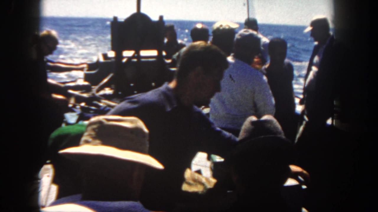Men gathered on a boat deck with fishing gear and open ocean beyond.