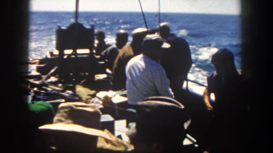 Men aboard a San Diego fishing boat in 1962 look toward rods and deck gear as the vessel leaves a wake on the sea.