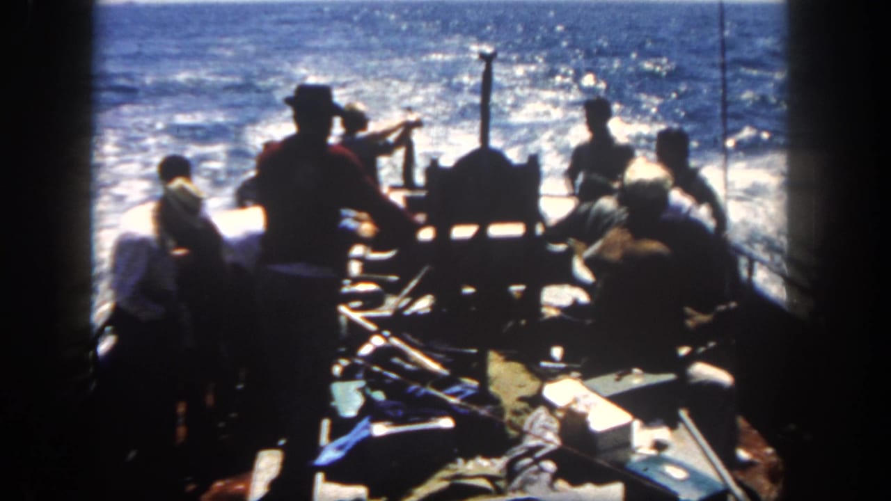 Several men stand and sit around the stern of a fishing boat in San Diego, California, in 1962, silhouetted against sunlit ocean water.