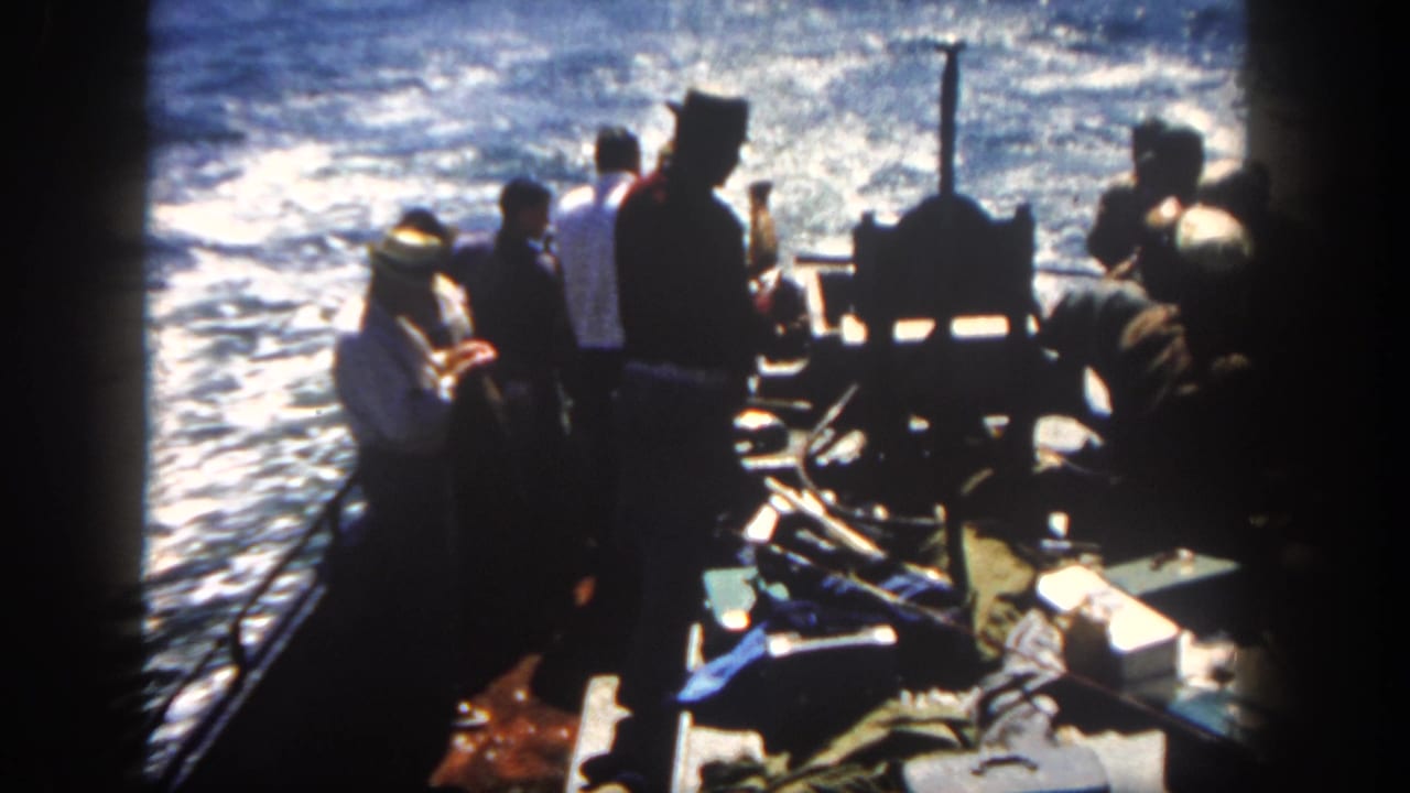 Passengers stand and sit on a small boat with choppy water behind them.