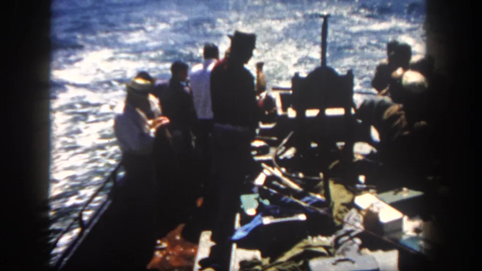 1962 San Diego 8mm frame showing silhouetted passengers on a small boat as foamy blue water trails behind.