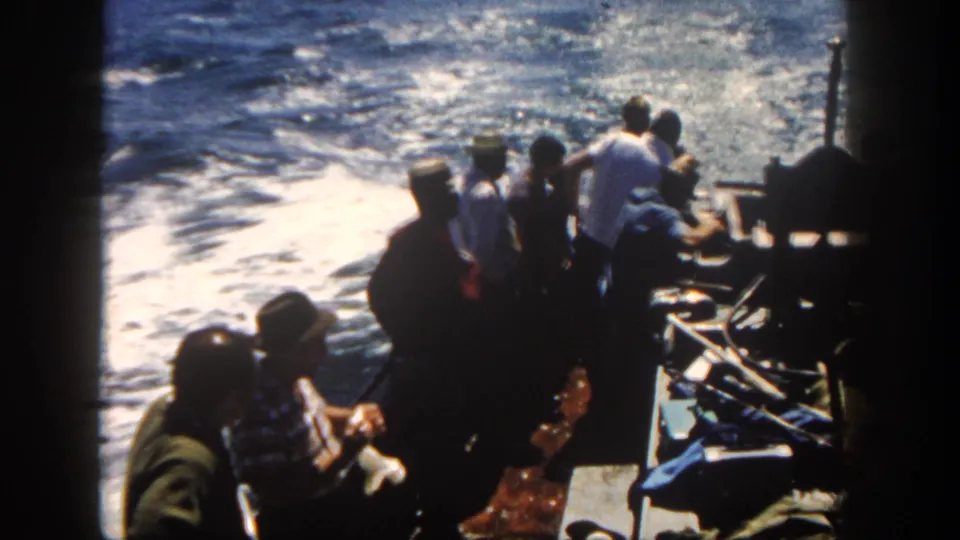 1962 San Diego boating scene with passengers silhouetted against sunlit, foamy water from an onboard 8mm view.