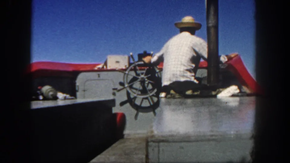 1962 San Diego home-movie frame showing the boat operator from behind at the wheel with open sky above.