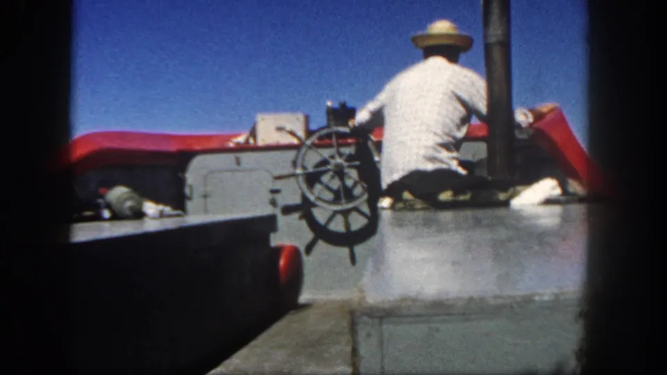 1962 San Diego frame of the boat operator at the wheel, with red trim, gray paneling, and clear sky visible.