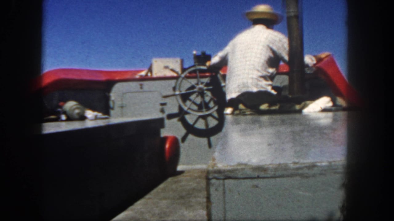 1962 San Diego 8mm frame showing a man in a straw hat steering from a boat deck under a blue sky.