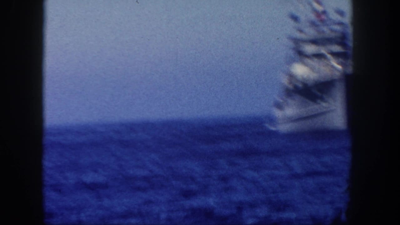 Gray naval ship partly seen beyond dark film-frame edges on open blue water.