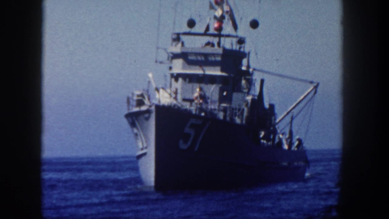 Naval ship with hull number 57 moving on calm ocean under a hazy sky.