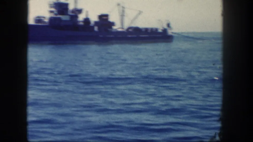 Wide 1962 8mm view of the naval vessel receding across open ocean, with its stern area, deck equipment, and horizon visible.