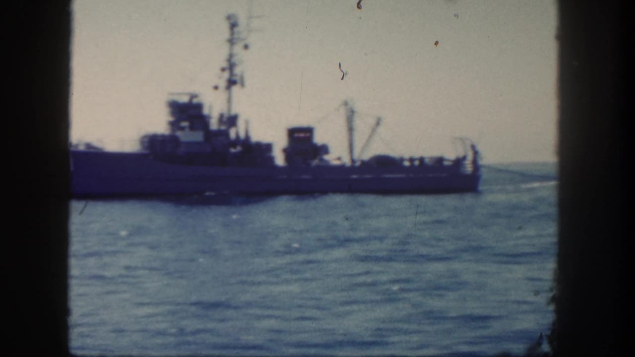 Naval ship at sea seen through dark window-like frame edges.