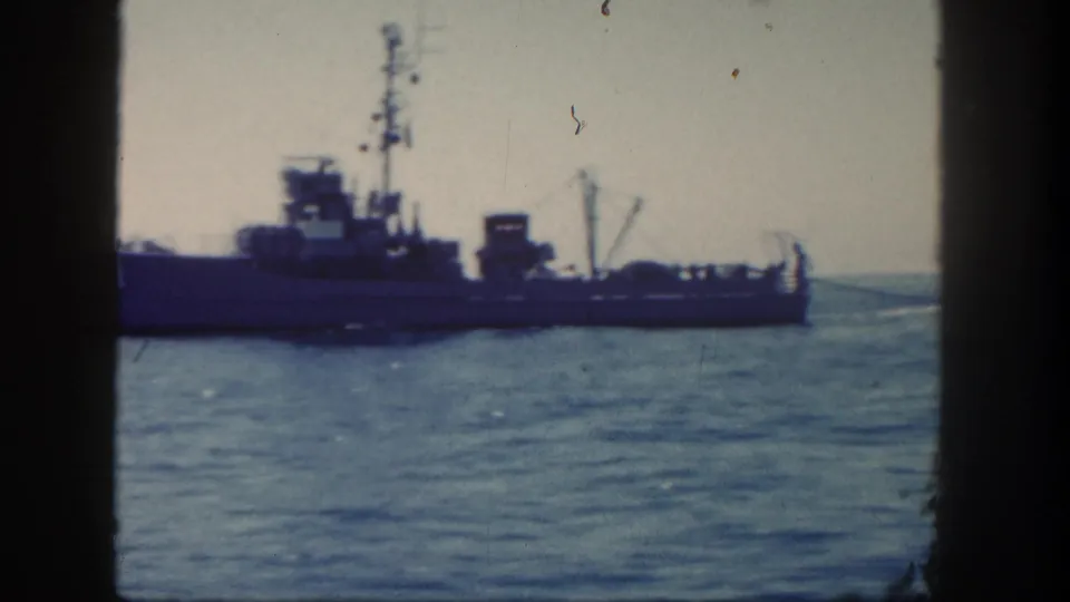 1962 San Diego-area 8mm frame showing a naval vessel on calm water through a dark vertical window or railing frame.