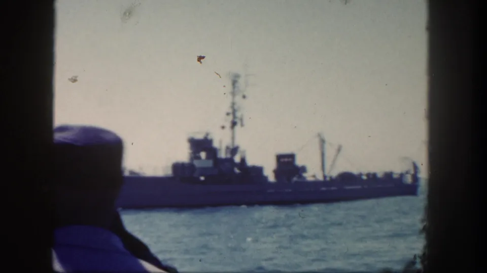 1962 home-movie frame with a sailor in cap seen from behind as a naval ship moves across the water near San Diego.