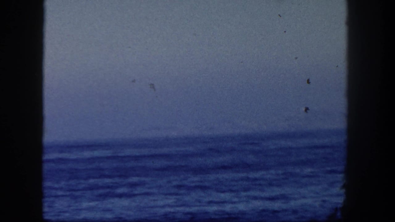 1962 San Diego 8mm frame showing rough ocean water and a distant horizon from a boat, with dark film-gate edges.