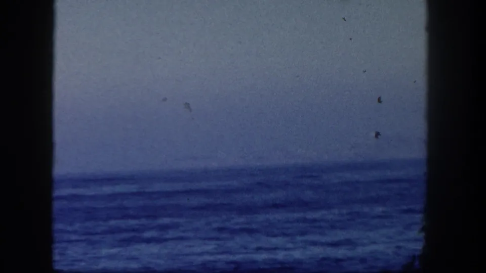 1962 San Diego 8mm frame showing rough ocean water and a distant horizon from a boat, with dark film-gate edges.