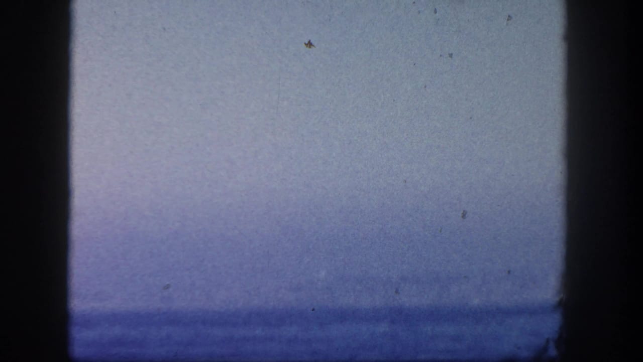 1962 San Diego boat-view frame with a pale sky, blurred ocean horizon, and prominent dark 8mm frame edges.
