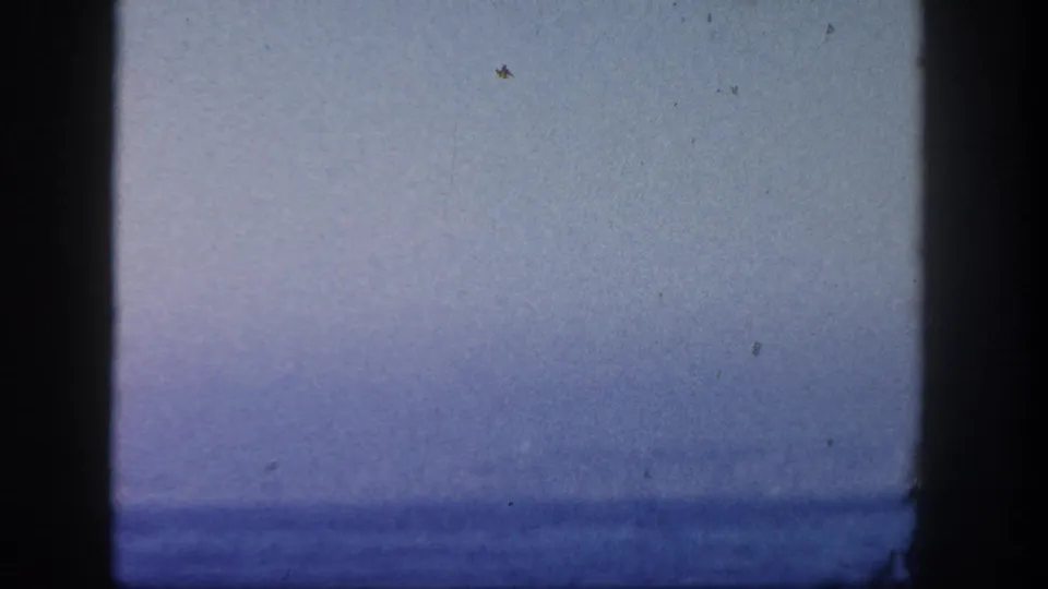 1962 San Diego boat-view frame with a pale sky, blurred ocean horizon, and prominent dark 8mm frame edges.