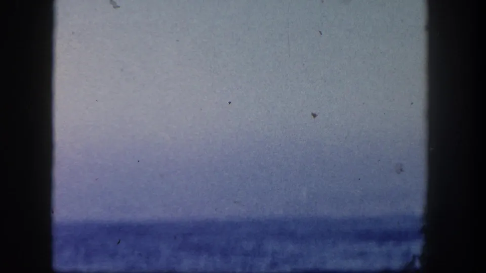 1962 San Diego 8mm frame showing a low, soft ocean horizon beneath a pale sky, with physical-film dust and edge shadows.