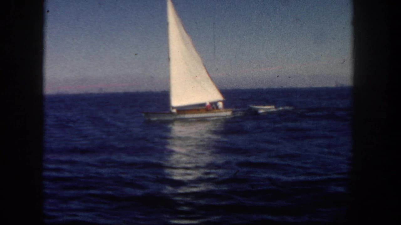 A small sailboat with a bright white sail moves across San Diego coastal waters in this 1962 home-movie frame.