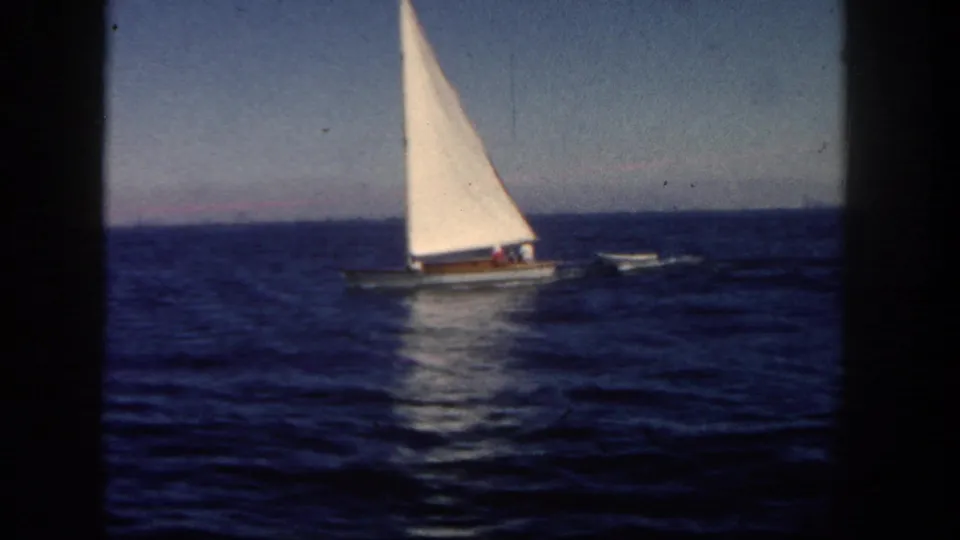 A small sailboat with a bright white sail moves across San Diego coastal waters in this 1962 home-movie frame.