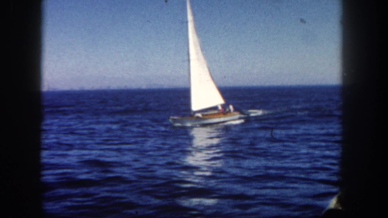 White sailboat crossing blue ocean under a clear sky, framed by dark film edges.