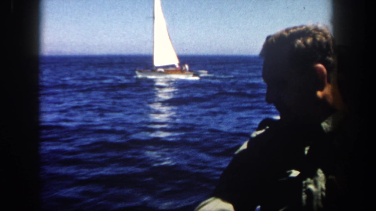 Sailboat on open water with a man in dark profile at the right edge.