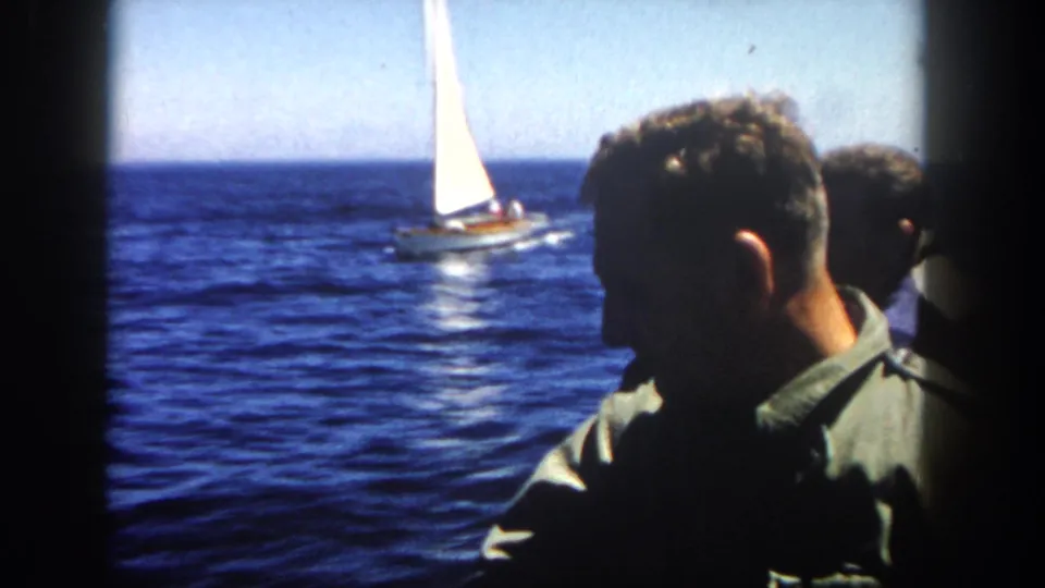 1962 San Diego home-movie view from a vessel, with an adult man in profile and a white sailboat beyond him on the ocean.