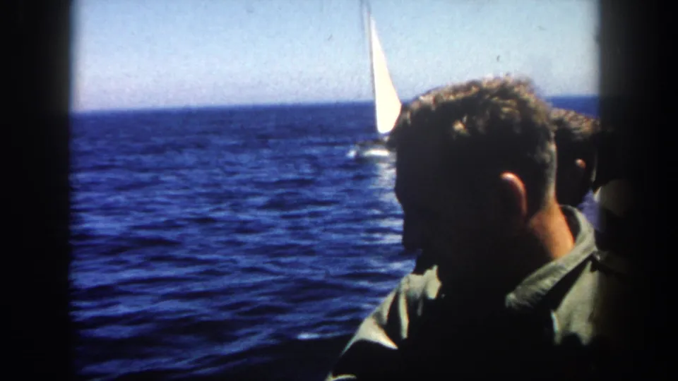 1962 San Diego frame showing shadowed adult profiles in the foreground and a small white-sailed boat on the ocean behind them.