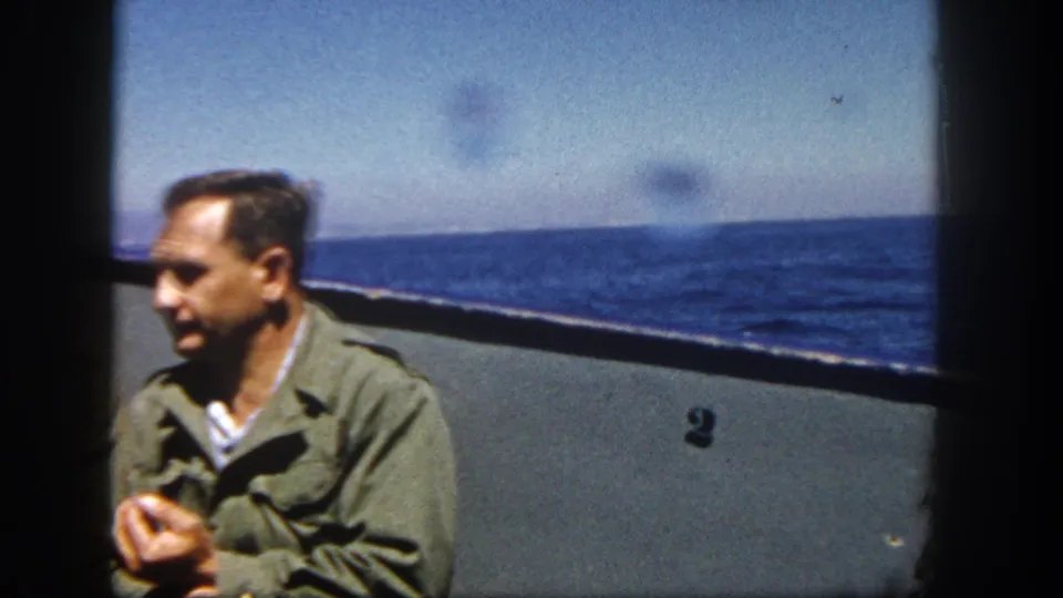 Adult man in a green jacket on a boat off San Diego in 1962, holding a small object as ocean and horizon fill the background.