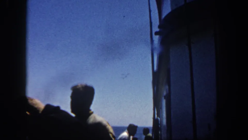 Home-movie frame from 1962 showing a silhouetted man at a ship deck opening, facing the San Diego-area ocean horizon.