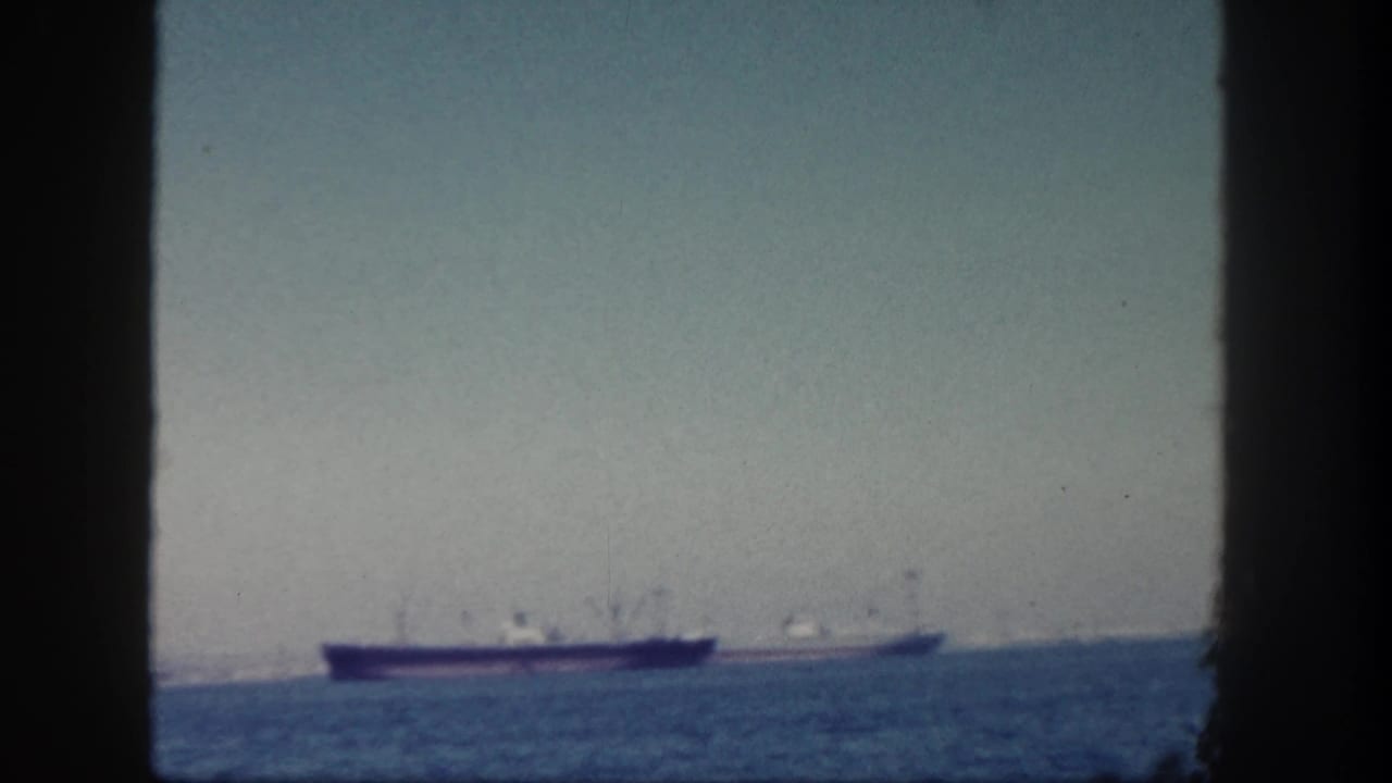 1962 San Diego home-movie frame showing two faraway cargo ships on the ocean through dark vertical edges.