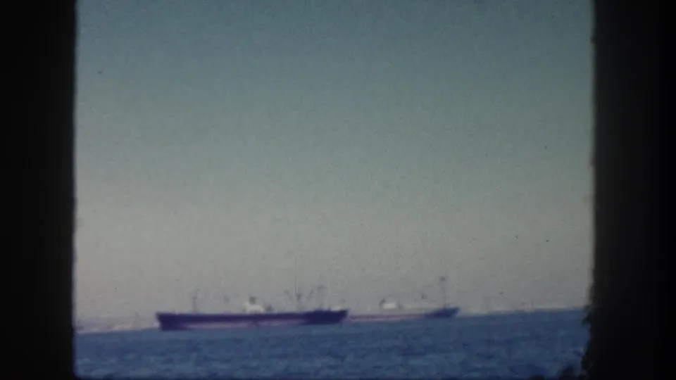 1962 San Diego home-movie frame showing two faraway cargo ships on the ocean through dark vertical edges.